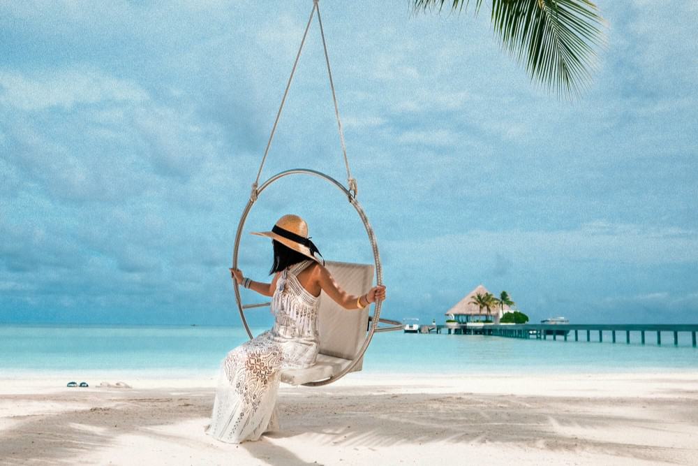 Eine äußerst luxuriöse Frau, die auf einer Schaukel am Strand sitzt und einen exklusiven Urlaub genießt.
