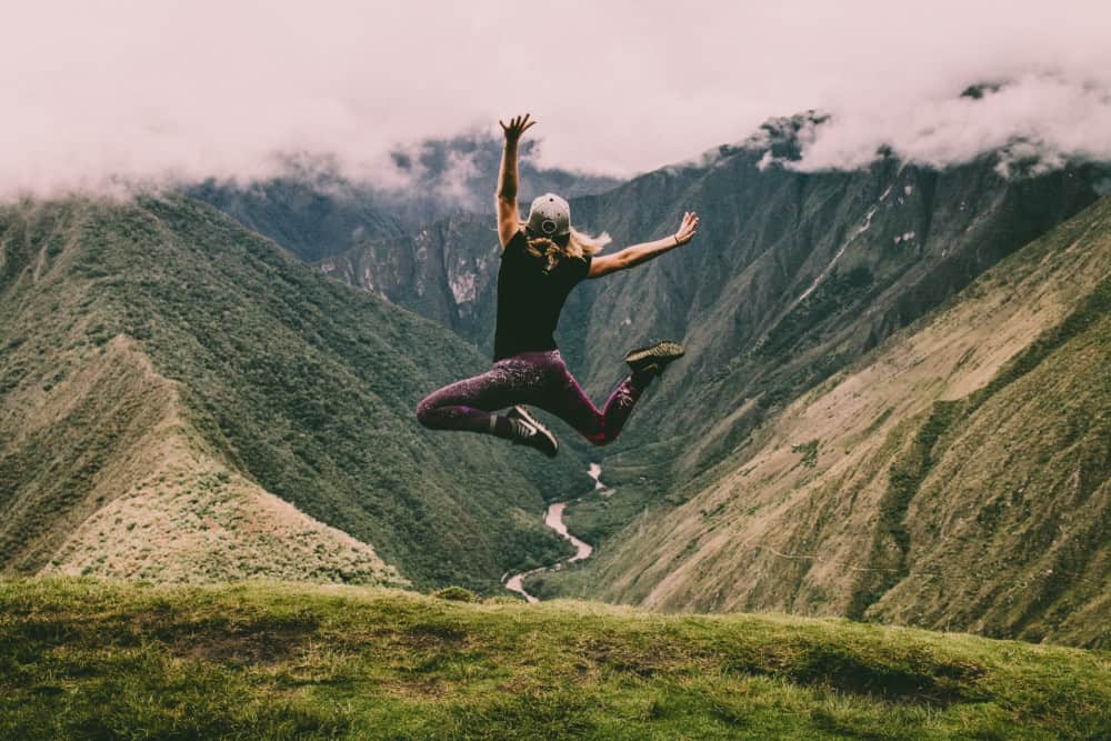 Eine Frau springt während eines exklusiven Reisen-Erlebnisses auf einem Berggipfel in die Luft.